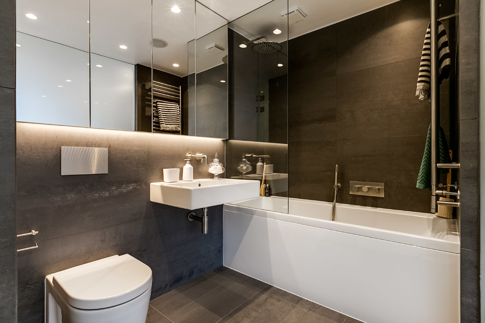 Photo of a small contemporary ensuite bathroom in London with a built-in bath, a shower/bath combination, a wall mounted toilet, black walls, cement flooring, a built-in sink, a hinged door, flat-panel cabinets and black floors.
