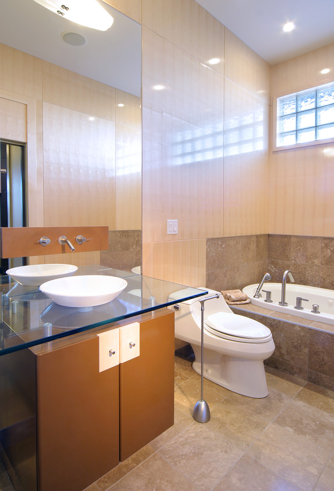 Idées déco pour une salle de bain contemporaine avec une vasque, un placard à porte plane, des portes de placard marrons, un plan de toilette en verre, une baignoire posée, WC à poser et un carrelage gris.