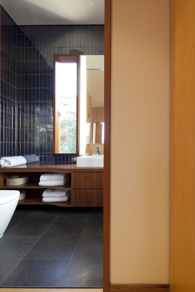 シドニーにあるコンテンポラリースタイルのおしゃれな浴室 (オーバーカウンターシンク、中間色木目調キャビネット、木製洗面台、黒いタイル) の写真