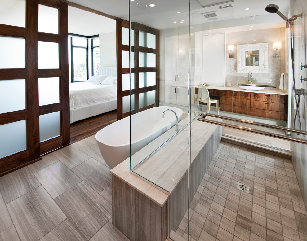 Modelo de cuarto de baño contemporáneo con lavabo sobreencimera, armarios con paneles lisos, puertas de armario de madera en tonos medios, bañera exenta y baldosas y/o azulejos grises