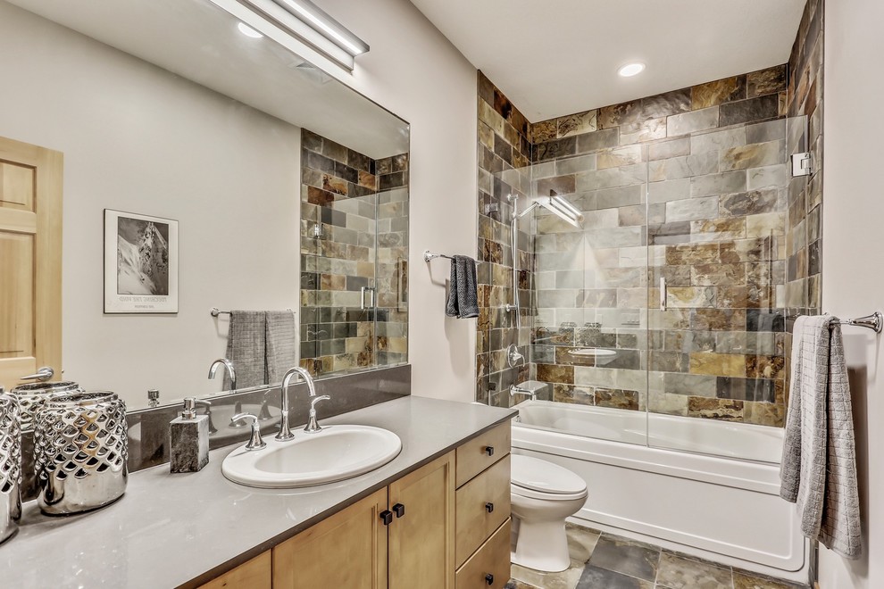 Photo of a medium sized traditional shower room bathroom in Calgary with beaded cabinets, grey walls, a built-in sink, engineered stone worktops, a hinged door, medium wood cabinets, an alcove bath, an alcove shower, a two-piece toilet, brown tiles, slate tiles, slate flooring and brown floors.