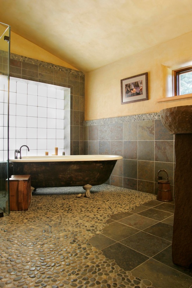 Cette image montre une salle de bain principale chalet avec une baignoire indépendante, une douche d'angle, un carrelage gris, un mur beige, un sol en galet et un carrelage de pierre.