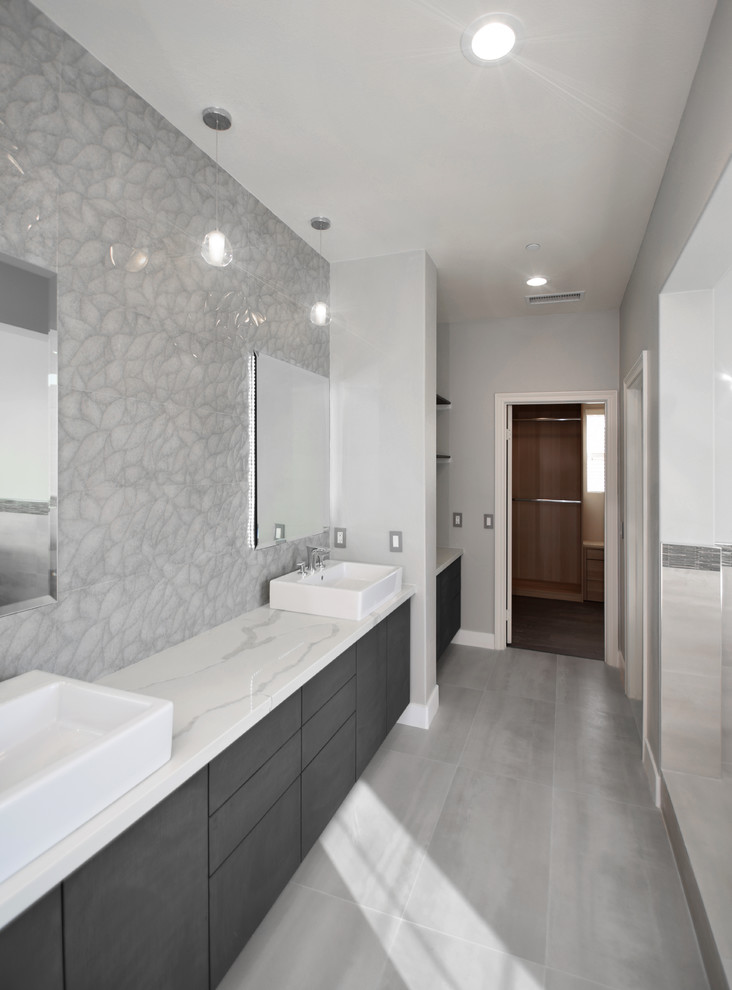Cette photo montre une grande salle de bain principale moderne avec un placard à porte plane, des portes de placard grises, une baignoire indépendante, un espace douche bain, un carrelage gris, des carreaux de porcelaine et un plan de toilette en quartz modifié.