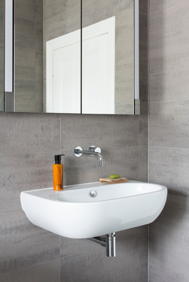 Cette image montre une salle de bain design de taille moyenne avec un carrelage gris, un mur gris, un lavabo suspendu, un placard à porte vitrée, WC séparés, un sol gris et meuble simple vasque.