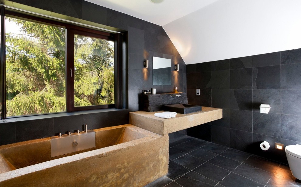 Cette photo montre une salle de bain principale tendance avec une baignoire posée, un carrelage noir, une vasque, un sol noir et un plan de toilette beige.