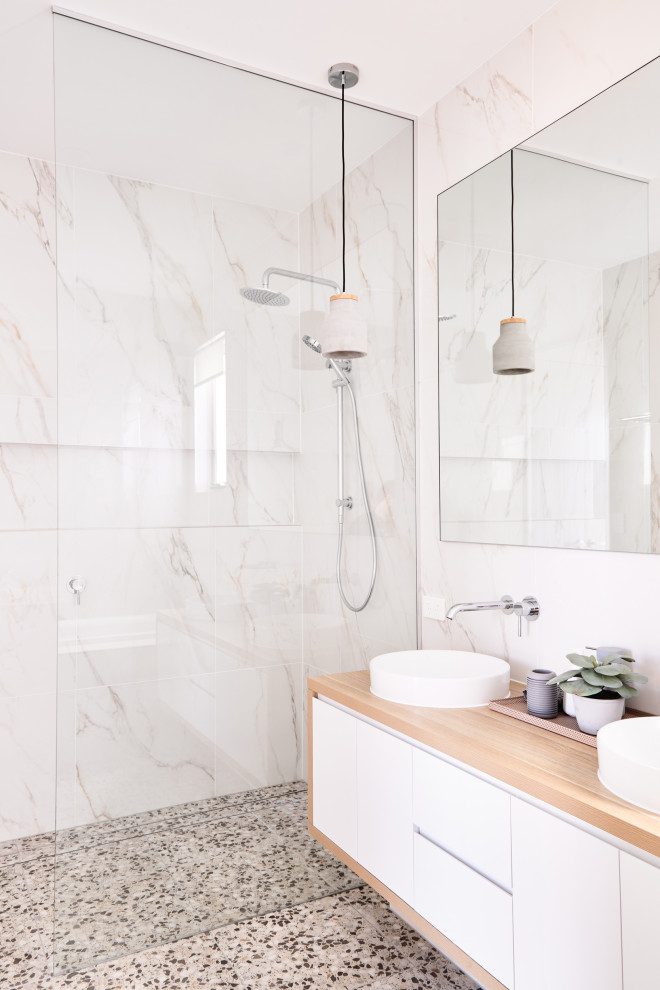 Modern inredning av ett beige beige badrum, med släta luckor, vita skåp, en dusch i en alkov, vit kakel, ett fristående handfat, träbänkskiva och grått golv