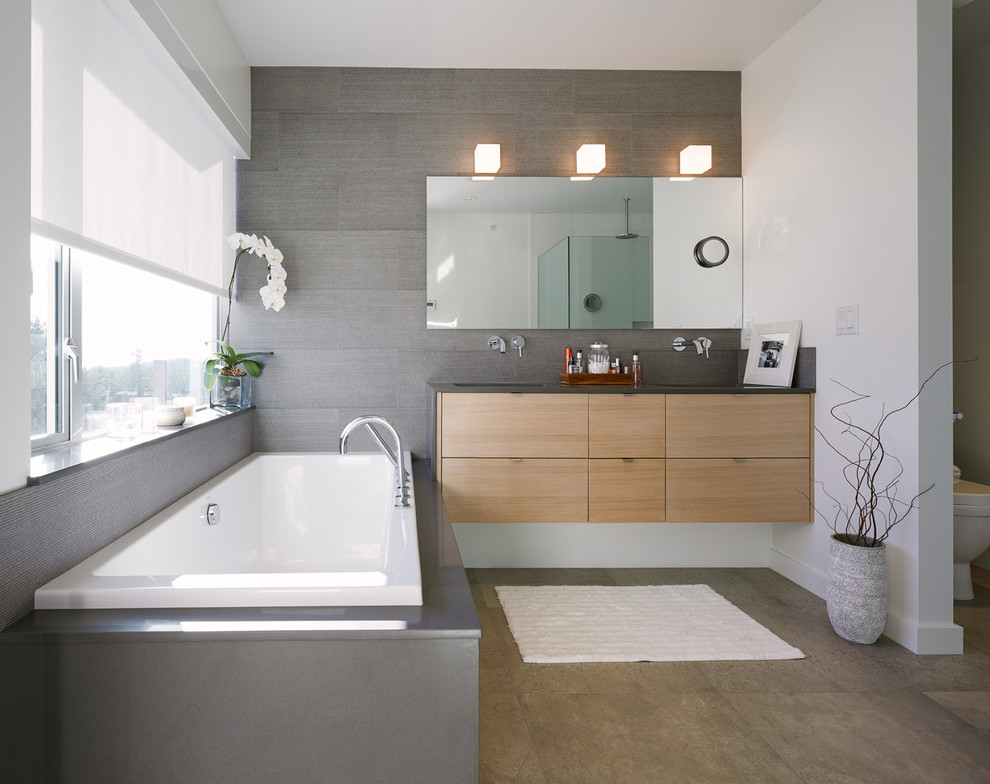 Diseño de cuarto de baño actual con puertas de armario de madera clara, bañera encastrada, baldosas y/o azulejos grises y paredes blancas