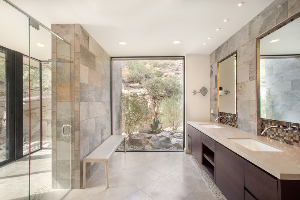 Inspiration for a large contemporary master glass tile and gray tile limestone floor walk-in shower remodel in Phoenix with flat-panel cabinets, dark wood cabinets, an undermount sink, solid surface countertops and gray walls