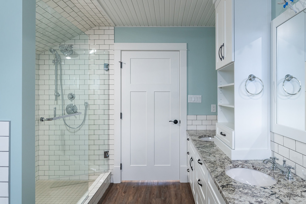 На фото: большая главная ванная комната в стиле кантри с фасадами в стиле шейкер, белыми фасадами, накладной ванной, двойным душем, унитазом-моноблоком, белой плиткой, керамической плиткой, синими стенами, полом из винила, врезной раковиной, столешницей из гранита, коричневым полом, душем с распашными дверями и разноцветной столешницей с