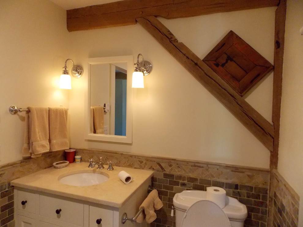 Example of a small farmhouse 3/4 beige tile and stone tile medium tone wood floor bathroom design in Burlington with shaker cabinets, white cabinets, a two-piece toilet, white walls, an undermount sink and solid surface countertops