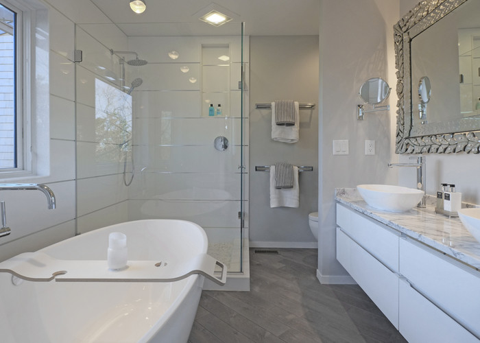 Idéer för mellanstora funkis en-suite badrum, med släta luckor, vita skåp, ett fristående badkar, en hörndusch, en toalettstol med hel cisternkåpa, vit kakel, porslinskakel, grå väggar, mellanmörkt trägolv, ett fristående handfat, marmorbänkskiva, grått golv och dusch med gångjärnsdörr