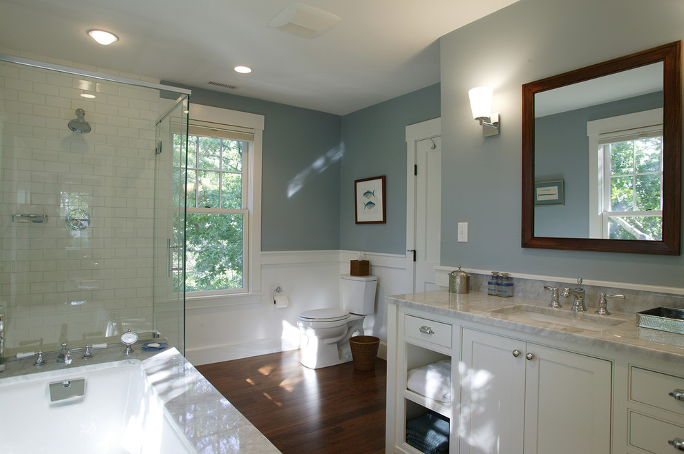 Inredning av ett klassiskt mellanstort en-suite badrum, med vita skåp, ett undermonterat badkar, en toalettstol med separat cisternkåpa, vit kakel, keramikplattor, blå väggar, mörkt trägolv, ett undermonterad handfat, marmorbänkskiva, luckor med profilerade fronter och en hörndusch