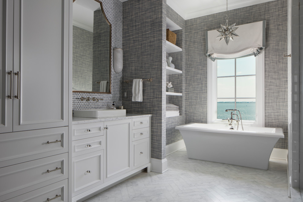 Diseño de cuarto de baño principal costero con armarios con paneles empotrados, puertas de armario blancas, bañera exenta, paredes grises, lavabo sobreencimera y suelo blanco