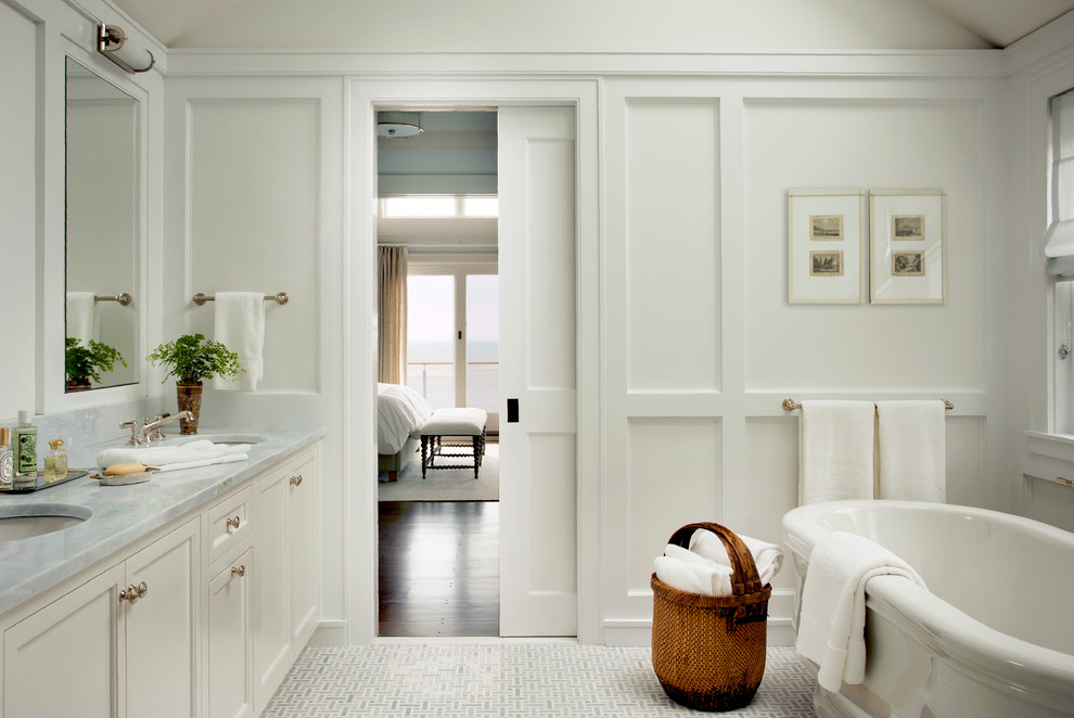 Idée de décoration pour une salle de bain tradition avec un placard avec porte à panneau encastré, des portes de placard blanches, une baignoire indépendante, un mur blanc, un lavabo encastré, un sol gris, un plan de toilette gris et une porte coulissante.