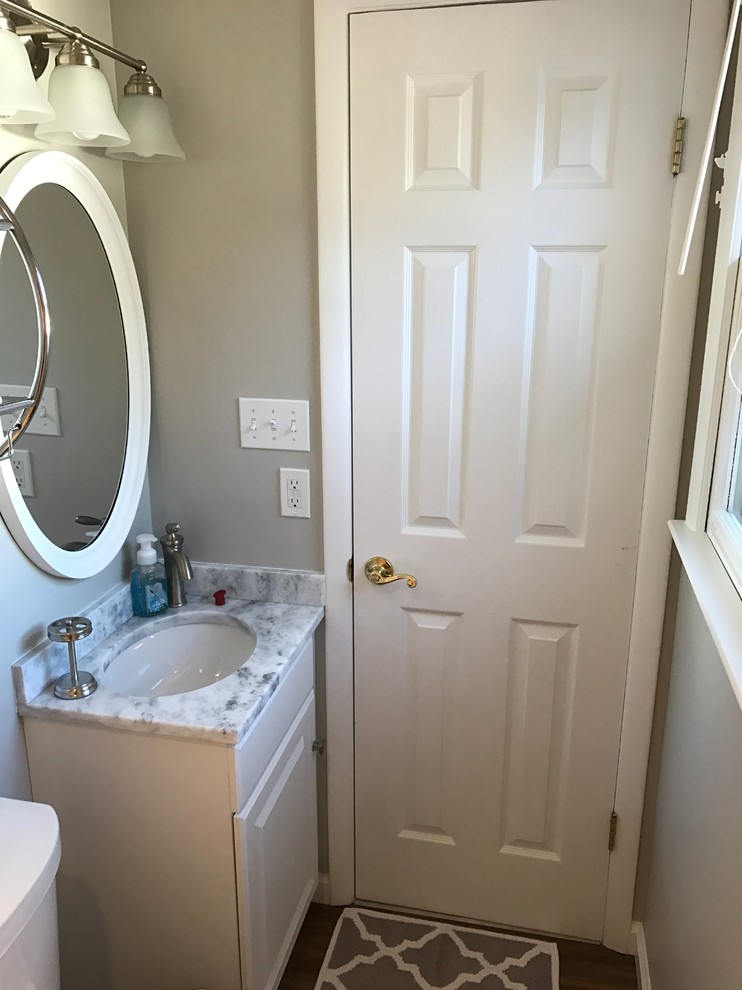 Cette photo montre une petite salle de bain tendance avec un placard avec porte à panneau surélevé, des portes de placard blanches, WC séparés, un carrelage blanc, des carreaux de céramique, un mur gris, un sol en carrelage de porcelaine, un lavabo encastré, un plan de toilette en marbre, un sol marron et une cabine de douche à porte coulissante.