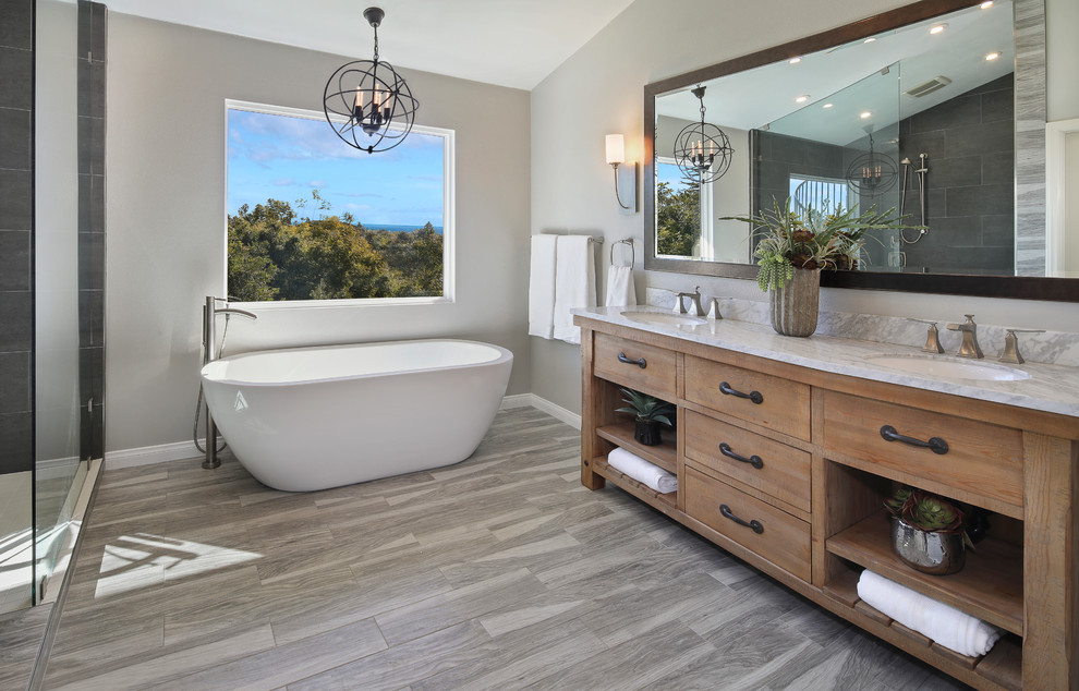 Example of a large transitional master porcelain tile and gray tile medium tone wood floor and gray floor bathroom design in Orange County with medium tone wood cabinets, gray walls, an undermount sink, a one-piece toilet, marble countertops and flat-panel cabinets