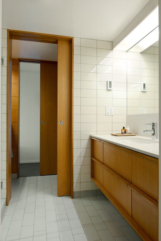 Exemple d'une salle de bain rétro en bois brun de taille moyenne avec un lavabo encastré, un placard à porte plane, un plan de toilette en surface solide, un carrelage blanc, des carreaux de béton, un mur blanc et un sol en carrelage de céramique.