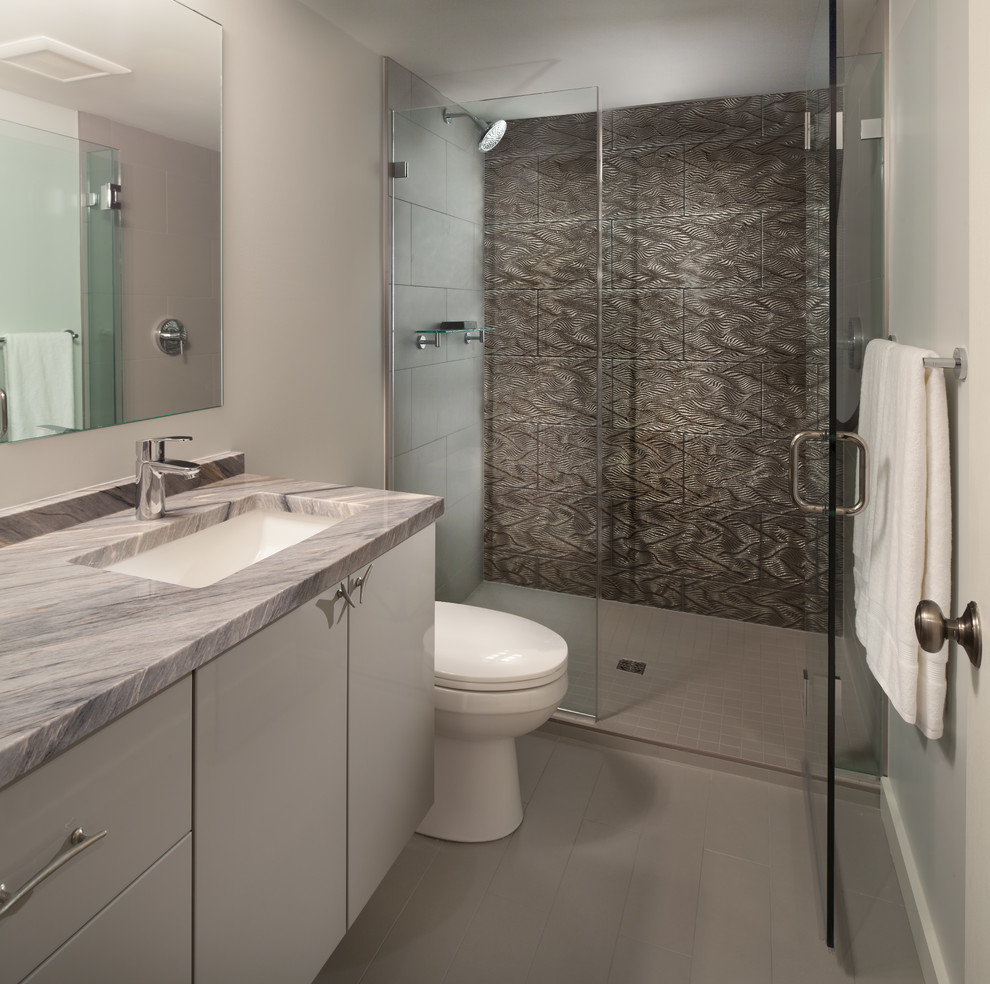 Exemple d'une salle de bain tendance de taille moyenne avec un placard à porte plane, des portes de placard grises, un carrelage gris, des carreaux de porcelaine, un mur gris, un sol en carrelage de porcelaine, un lavabo encastré, un plan de toilette en marbre et WC séparés.