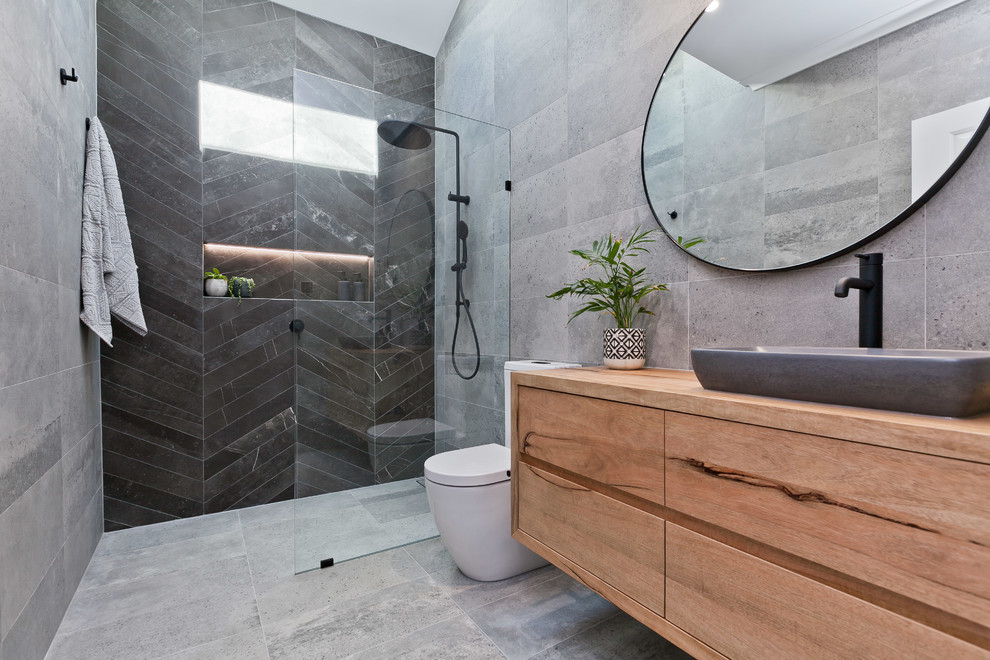 Idéer för att renovera ett stort funkis badrum, med släta luckor, en öppen dusch, en toalettstol med separat cisternkåpa, grå kakel, porslinskakel, grå väggar, klinkergolv i porslin, ett fristående handfat, träbänkskiva, grått golv och med dusch som är öppen