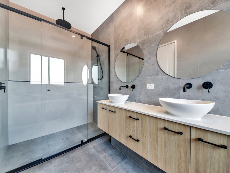 Inspiration for a small modern ensuite bathroom in Brisbane with flat-panel cabinets, light wood cabinets, a corner shower, a one-piece toilet, grey tiles, metro tiles, white walls, porcelain flooring, a vessel sink, granite worktops, grey floors, a hinged door and white worktops.