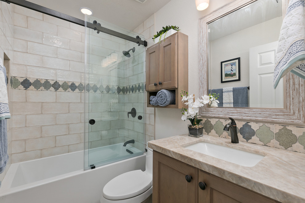 This is an example of a small traditional family bathroom in San Diego with shaker cabinets, brown cabinets, an alcove bath, a shower/bath combination, a one-piece toilet, white tiles, porcelain tiles, beige walls, vinyl flooring, a submerged sink, quartz worktops, brown floors, a sliding door, beige worktops, a single sink and a built in vanity unit.