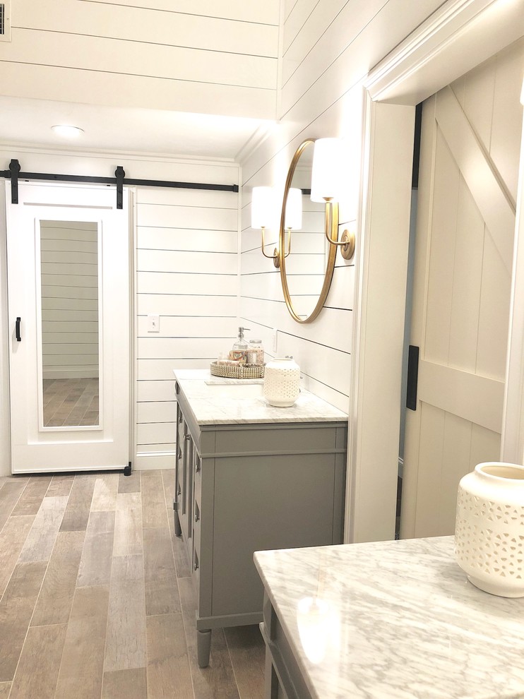 Photo of a large rural ensuite bathroom in Bridgeport with recessed-panel cabinets, grey cabinets, white walls, light hardwood flooring, a submerged sink, granite worktops, brown floors and white worktops.