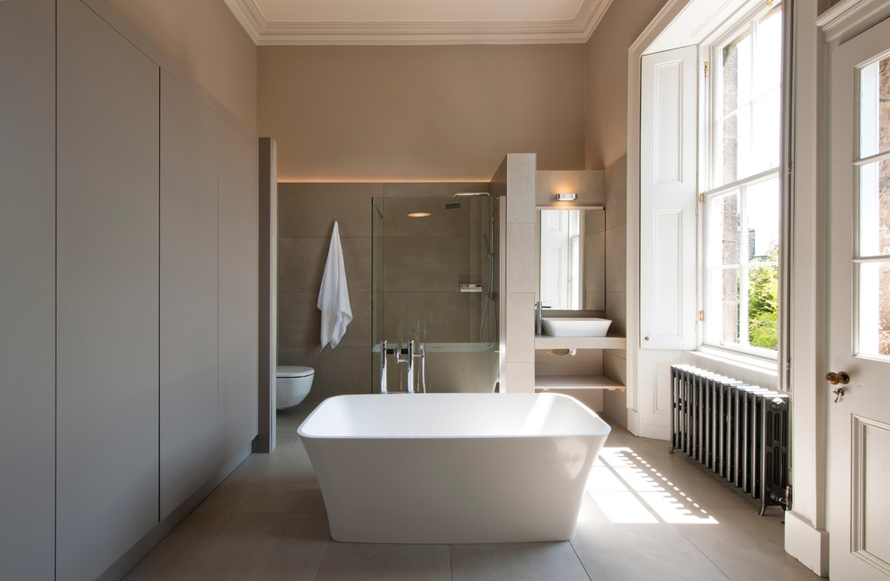 Foto på ett stort funkis en-suite badrum, med ett fristående badkar, en öppen dusch, en vägghängd toalettstol, beige kakel, porslinskakel, beige väggar, klinkergolv i porslin, beiget golv och med dusch som är öppen