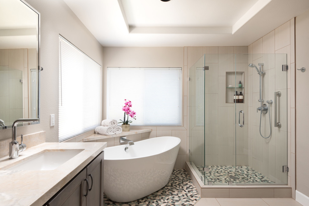 This is an example of a medium sized modern ensuite bathroom in San Diego with flat-panel cabinets, grey cabinets, a freestanding bath, a corner shower, a two-piece toilet, beige tiles, porcelain tiles, beige walls, porcelain flooring, a submerged sink and granite worktops.