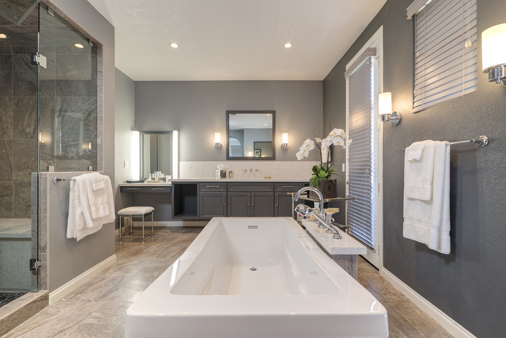 This is an example of an expansive modern ensuite bathroom in San Diego with a submerged sink, recessed-panel cabinets, grey cabinets, engineered stone worktops, a freestanding bath, a built-in shower, a one-piece toilet, beige tiles, stone tiles, grey walls and marble flooring.