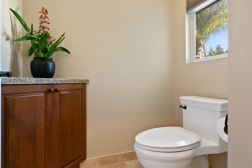 Exemple d'un très grand WC et toilettes chic en bois foncé avec un placard avec porte à panneau surélevé, WC à poser, un carrelage beige, un carrelage de pierre, un mur beige, un sol en carrelage de porcelaine, un lavabo encastré, un plan de toilette en granite, un sol beige et un plan de toilette marron.