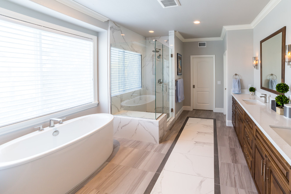 Design ideas for a large traditional ensuite bathroom in San Diego with raised-panel cabinets, dark wood cabinets, a freestanding bath, a corner shower, a two-piece toilet, white tiles, stone slabs, grey walls, porcelain flooring, an integrated sink, engineered stone worktops, multi-coloured floors, a hinged door and beige worktops.