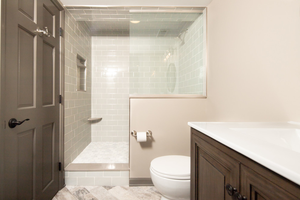 Bathroom - mid-sized transitional gray tile and subway tile limestone floor and gray floor bathroom idea in Indianapolis with furniture-like cabinets, medium tone wood cabinets, a two-piece toilet, beige walls, an integrated sink, solid surface countertops and white countertops