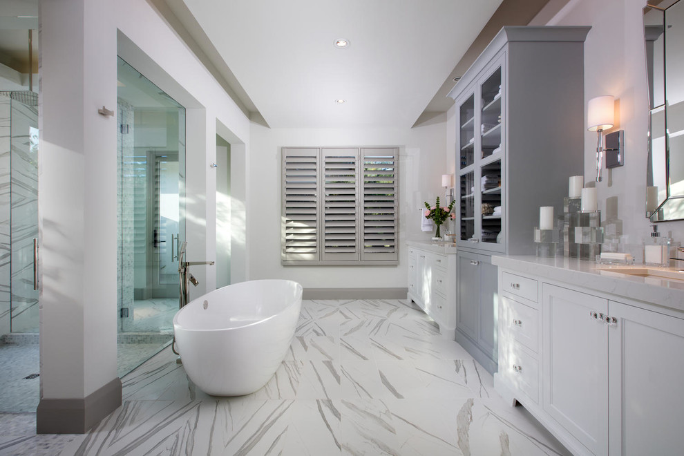 Klassisk inredning av ett en-suite badrum, med grå skåp, ett fristående badkar, en kantlös dusch, vita väggar, ett undermonterad handfat, flerfärgat golv, dusch med gångjärnsdörr och luckor med infälld panel