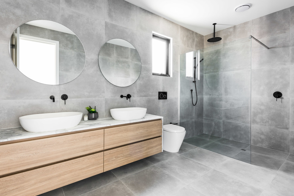 Inspiration för mellanstora moderna grått en-suite badrum, med släta luckor, en kantlös dusch, en toalettstol med hel cisternkåpa, grå väggar, ett fristående handfat, marmorbänkskiva, grått golv, skåp i ljust trä, grå kakel, cementkakel, betonggolv och med dusch som är öppen