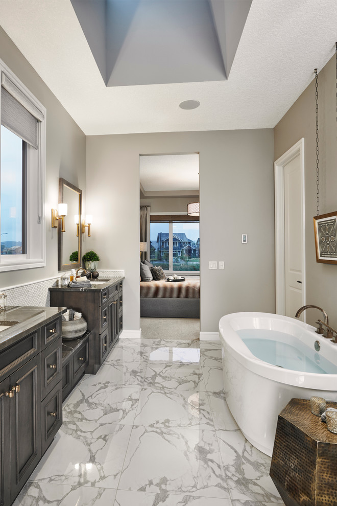 Traditional ensuite bathroom in Calgary with a submerged sink, recessed-panel cabinets, dark wood cabinets, marble worktops, a freestanding bath, a built-in shower, a one-piece toilet, white tiles, ceramic tiles, beige walls and ceramic flooring.