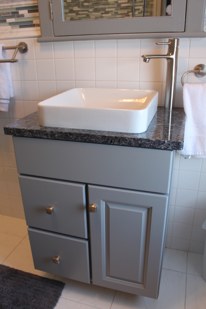 Modern inredning av ett litet badrum, med ett fristående handfat, luckor med upphöjd panel, grå skåp, granitbänkskiva, en toalettstol med separat cisternkåpa, vit kakel, porslinskakel, grå väggar och klinkergolv i porslin