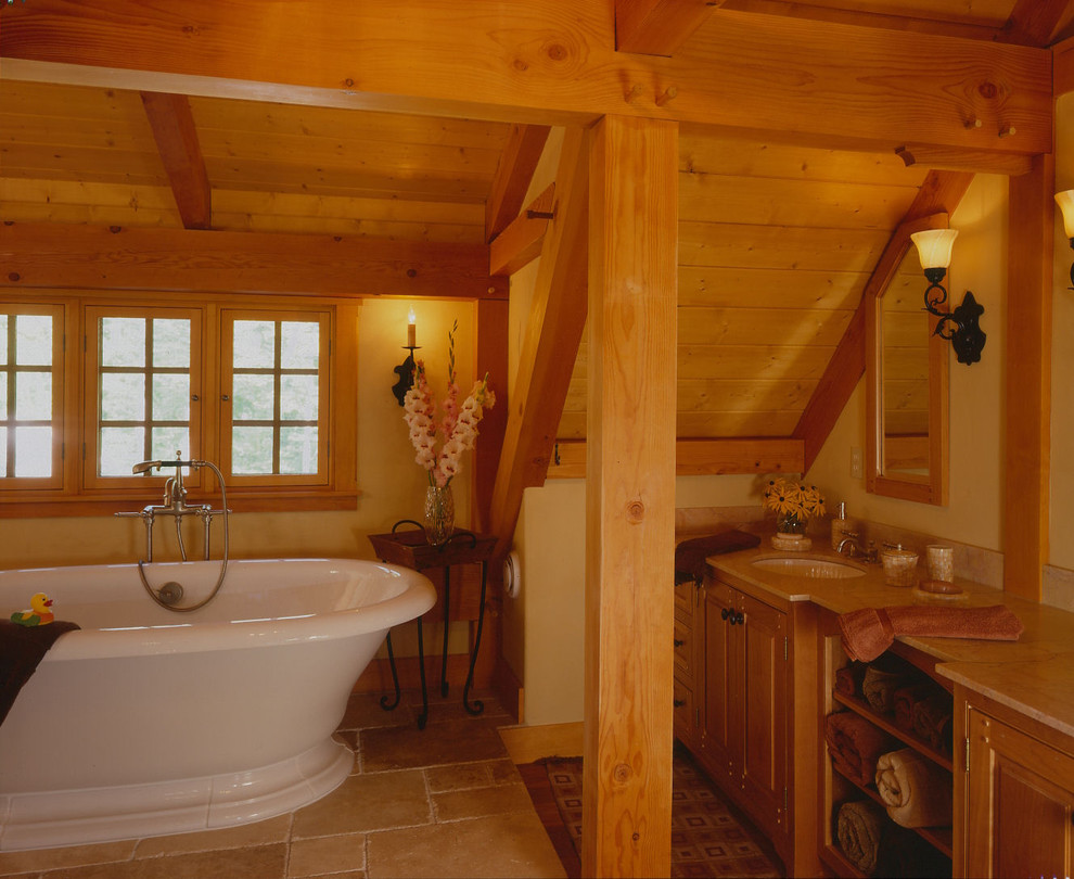 Klassisk inredning av ett en-suite badrum, med skåp i mellenmörkt trä, ett fristående badkar, beige kakel, gula väggar, ett nedsänkt handfat och luckor med upphöjd panel