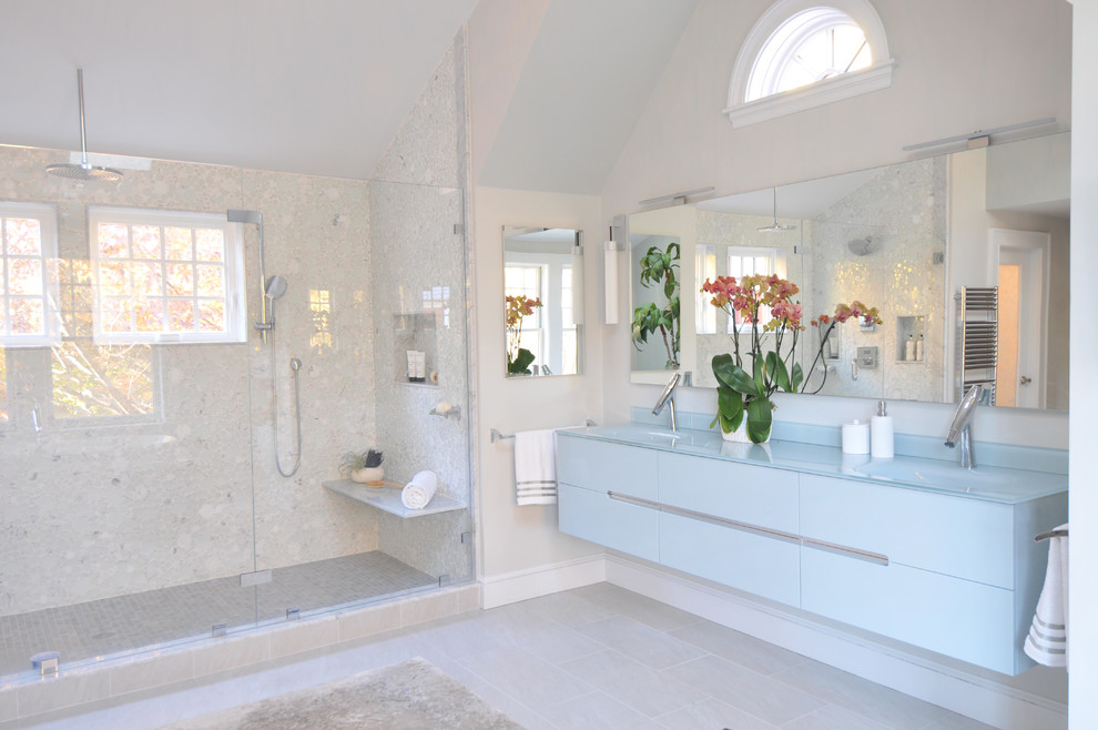 Inspiration för stora moderna blått en-suite badrum, med blå skåp, ett fristående badkar, en toalettstol med hel cisternkåpa, vit kakel, glaskakel, ett integrerad handfat, bänkskiva i glas, beiget golv, dusch med gångjärnsdörr, släta luckor, en dusch i en alkov, grå väggar och klinkergolv i porslin