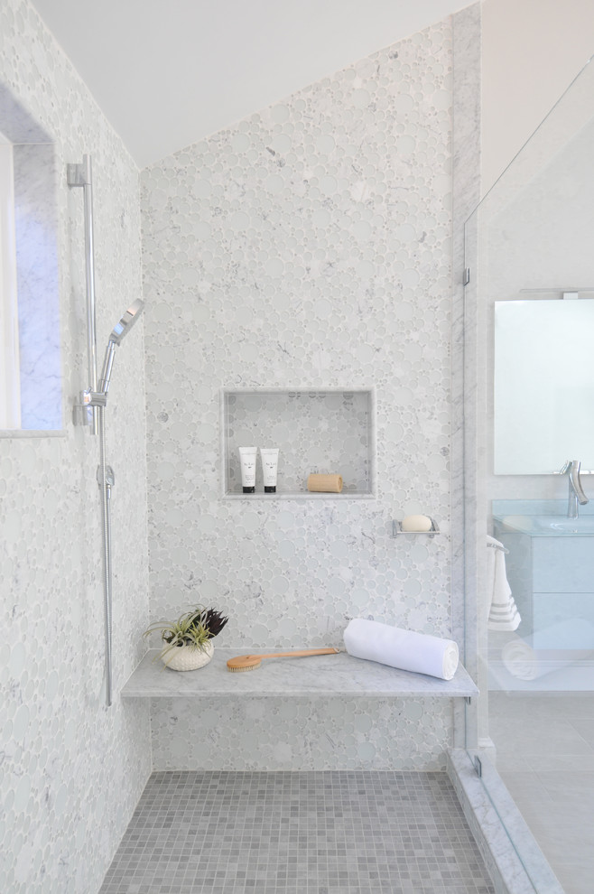 Пример оригинального дизайна: большая главная ванная комната в современном стиле с синими фасадами, отдельно стоящей ванной, унитазом-моноблоком, белой плиткой, стеклянной плиткой, монолитной раковиной, стеклянной столешницей, бежевым полом, душем с распашными дверями, синей столешницей, плоскими фасадами, душем в нише, серыми стенами и полом из керамогранита