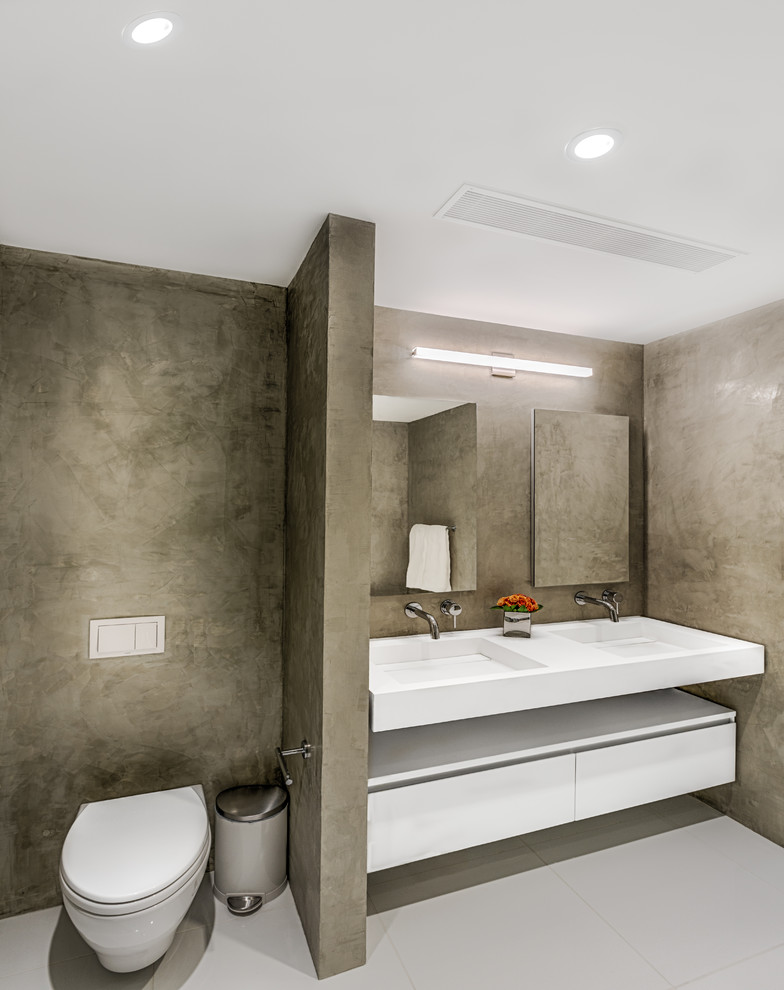 Cette photo montre une salle de bain principale tendance de taille moyenne avec un placard à porte plane, des portes de placard blanches, WC à poser, un mur gris, un lavabo suspendu, une baignoire indépendante, une douche ouverte et un plan de toilette blanc.