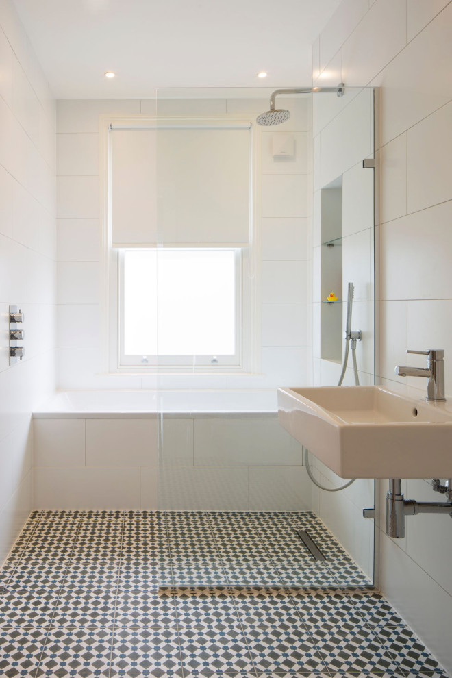 Пример оригинального дизайна: маленькая детская ванная комната с накладной ванной, открытым душем, унитазом-моноблоком, белой плиткой, керамической плиткой, белыми стенами, полом из мозаичной плитки, подвесной раковиной, разноцветным полом, открытым душем, тумбой под одну раковину и подвесной тумбой для на участке и в саду
