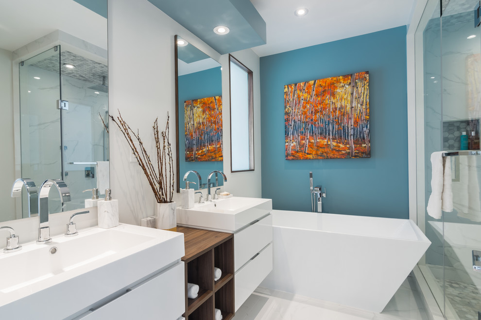Cette image montre une salle de bain principale design avec des portes de placard blanches, une baignoire indépendante, une douche d'angle, WC à poser, un carrelage blanc, des carreaux de porcelaine, un mur bleu, un sol en carrelage de porcelaine et une vasque.