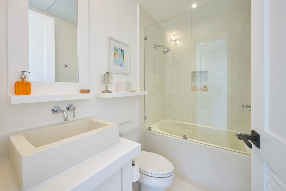 Inspiration for a medium sized coastal ensuite bathroom in Other with freestanding cabinets, white cabinets, an alcove bath, a shower/bath combination, a one-piece toilet, white tiles, cement tiles, white walls, cement flooring, a trough sink, concrete worktops, white floors, a hinged door and white worktops.