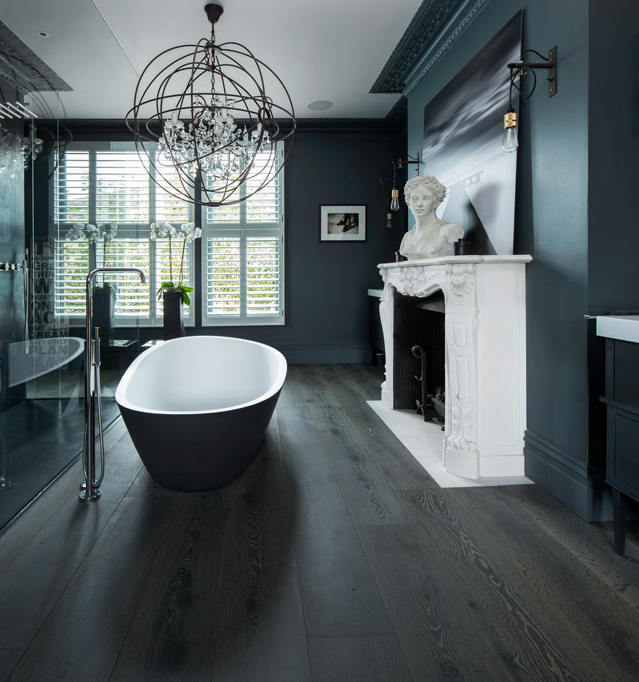 This is an example of a medium sized eclectic ensuite bathroom in London with freestanding cabinets, black cabinets, a freestanding bath, a walk-in shower, a wall mounted toilet, grey walls, dark hardwood flooring and a console sink.