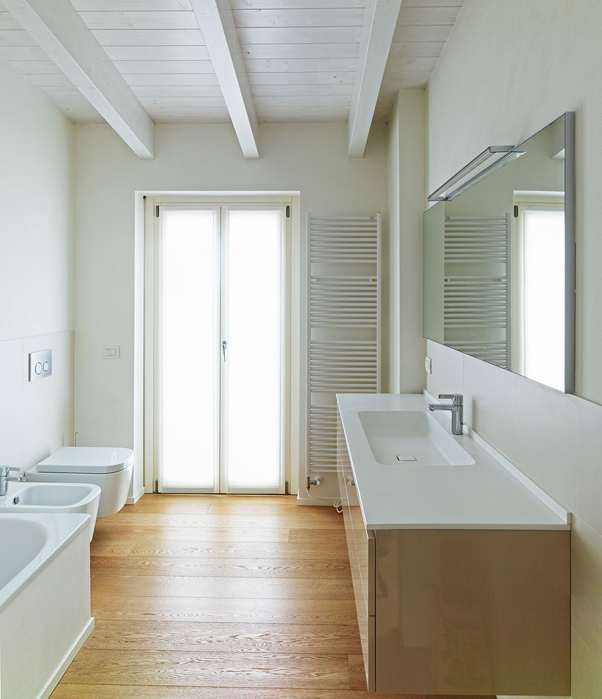 Modernes Badezimmer mit Einbaubadewanne, Wandtoilette, weißer Wandfarbe, hellem Holzboden und integriertem Waschbecken in Mailand