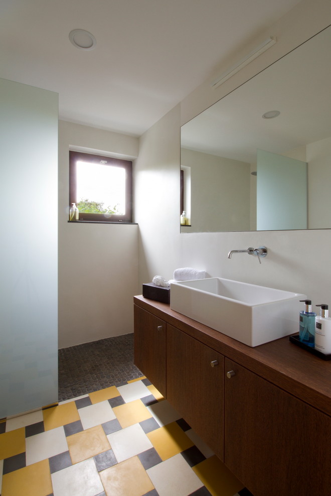 Inspiration for a small contemporary ensuite bathroom in Other with a vessel sink, flat-panel cabinets, dark wood cabinets, wooden worktops, a corner shower, a wall mounted toilet, orange tiles, cement tiles, white walls and ceramic flooring.