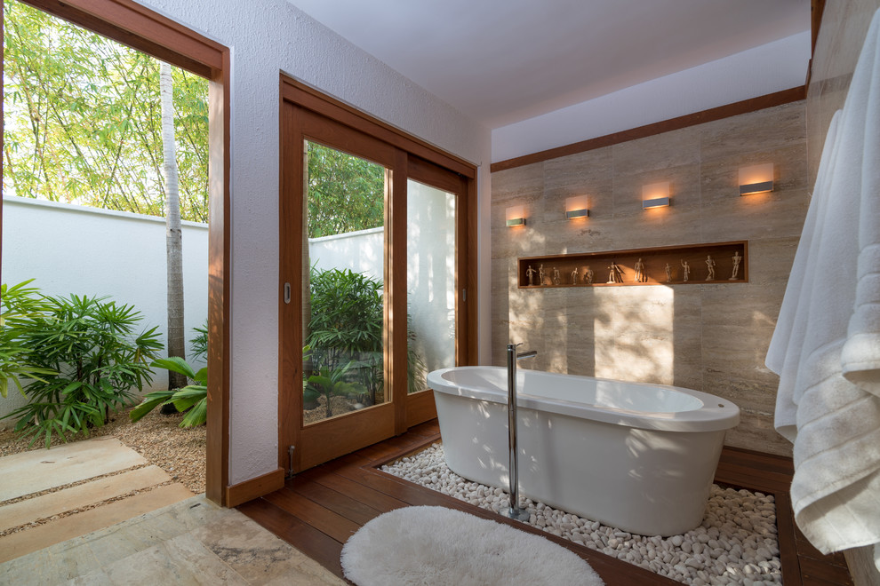 Imagen de cuarto de baño tropical con bañera exenta, baldosas y/o azulejos beige, paredes blancas y suelo de madera oscura