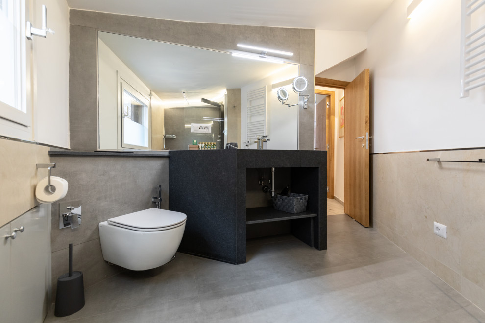 Inredning av ett modernt stort grå grått en-suite badrum, med öppna hyllor, grå skåp, en dubbeldusch, en vägghängd toalettstol, grå kakel, porslinskakel, grå väggar, klinkergolv i porslin, ett konsol handfat, granitbänkskiva, grått golv och dusch med skjutdörr