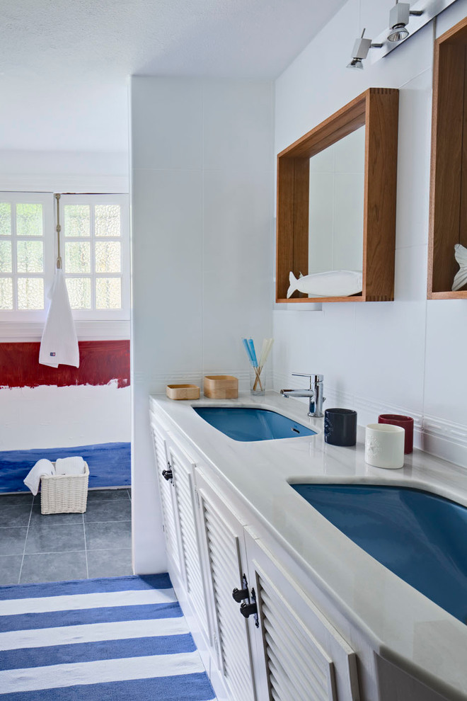 Cette photo montre une salle d'eau bord de mer de taille moyenne avec un lavabo encastré, un placard à porte persienne, des portes de placard blanches, un mur blanc, un sol en carrelage de céramique, un plan de toilette en marbre et un plan de toilette gris.