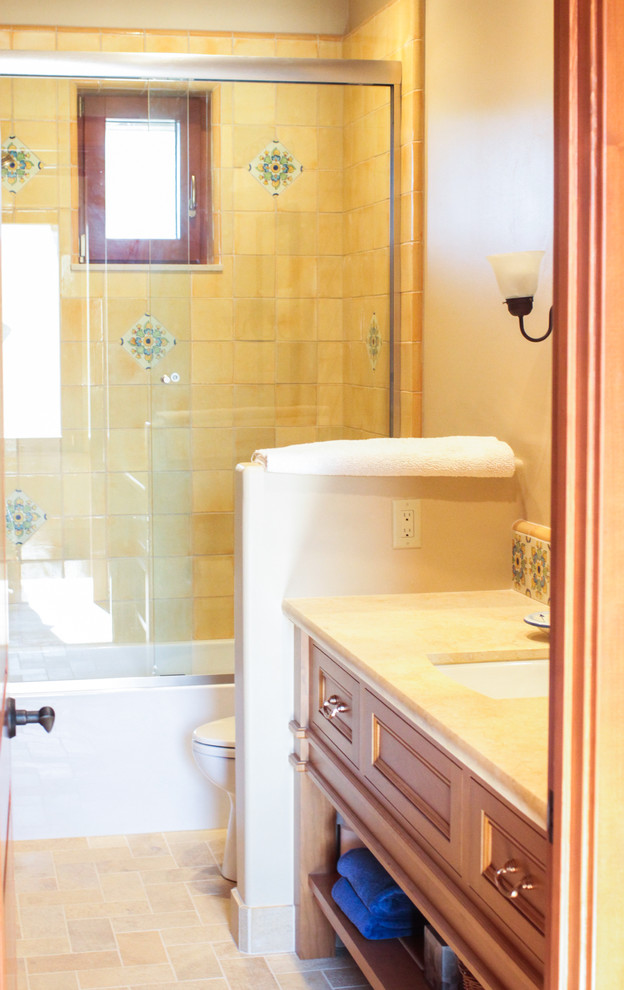 This is an example of a medium sized mediterranean ensuite bathroom in San Francisco with shaker cabinets, medium wood cabinets, an alcove bath, a shower/bath combination, a two-piece toilet, beige tiles, stone tiles, beige walls, medium hardwood flooring, a submerged sink, granite worktops, brown floors and a sliding door.